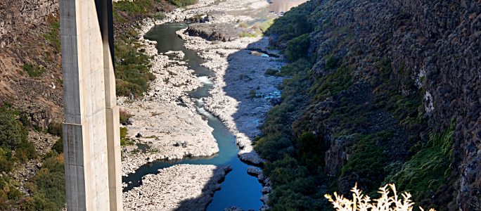 [From this view the river appears to be a stream flowing through rocky ground. Water level is down so much of the rocky riverbed is visible.]